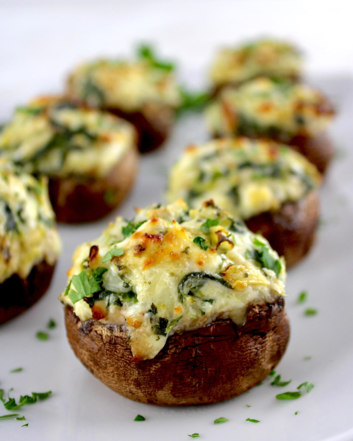 closeup of Spinach Artichoke Stuffed Mushrooms on white plate with parsley
