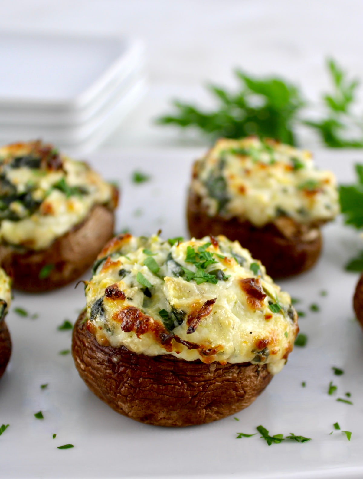 closeup of Spinach Artichoke Stuffed Mushrooms on white plate with parsley