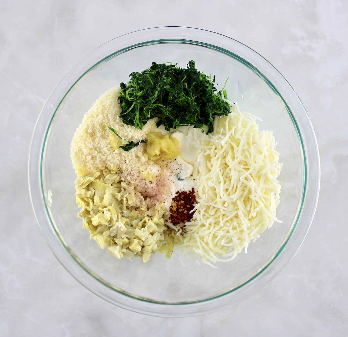 spinach artichoke filling ingredients unmixed in glass bowl