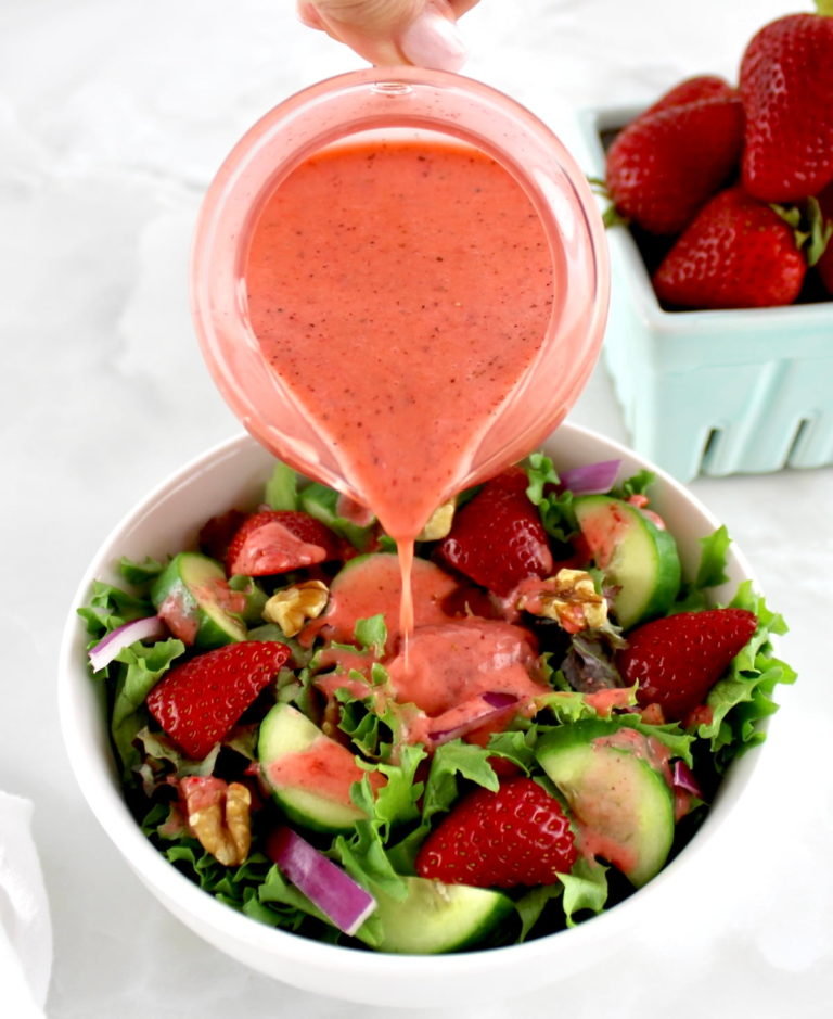 Strawberry Vinaigrette in glass pitcher being poured over salad in white bowl