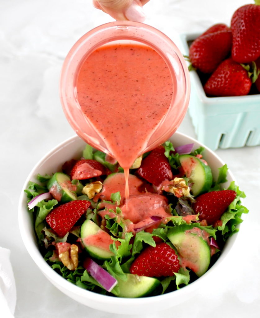 Strawberry Vinaigrette in glass pitcher being poured over salad in white bowl