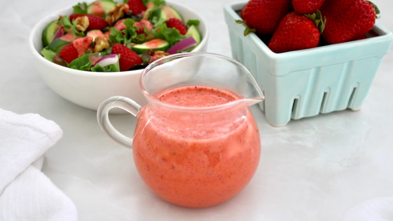 Strawberry Vinaigrette in glass pitcher with salad and strawberries in back