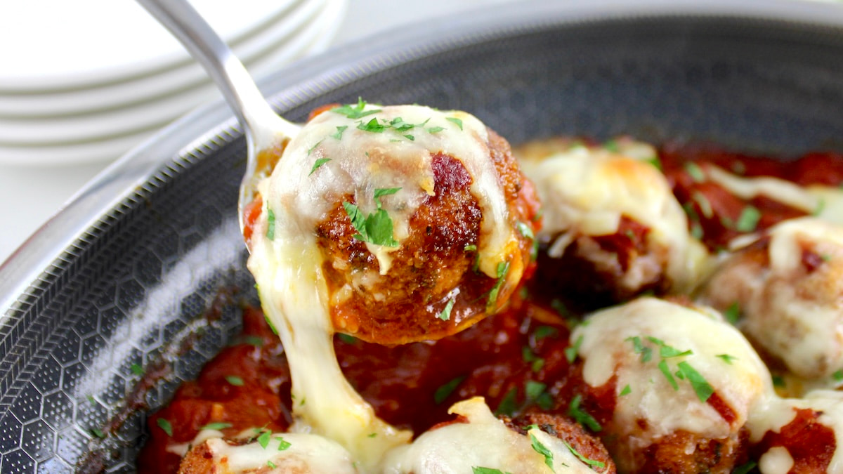 holding up Chicken Parmesan Meatball in spoon over skillet