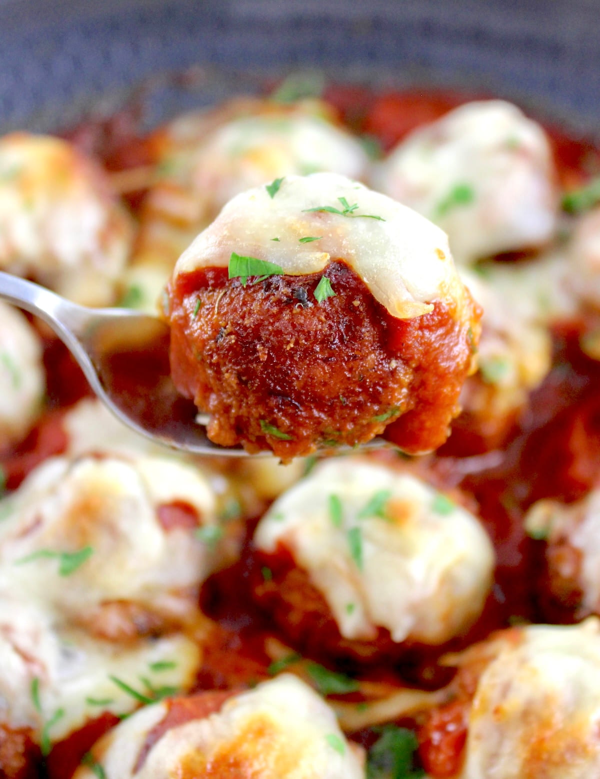 holding up Chicken Parmesan Meatball on fork over skillet
