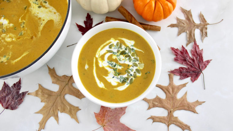 overhead view of Easy Pumpkin Soup in white bowl with pumpkins and fall leaves in back