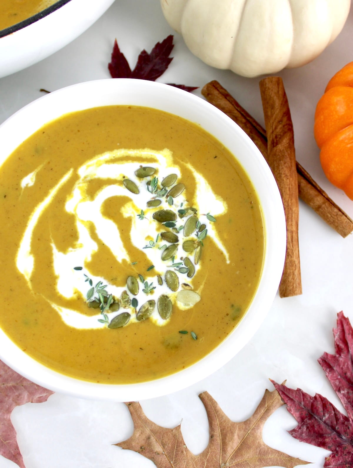 overhead view of Easy Pumpkin Soup in white bowl with pumpkins and fall leaves in back