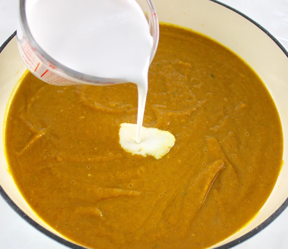 cream being poured into Easy Pumpkin Soup in pot