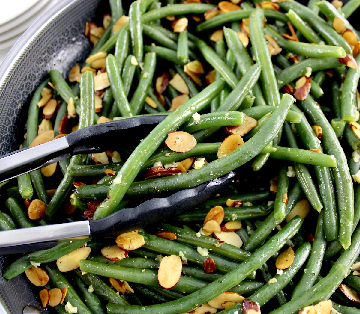 closeup of Green Beans Almondine in skillet with black tongs