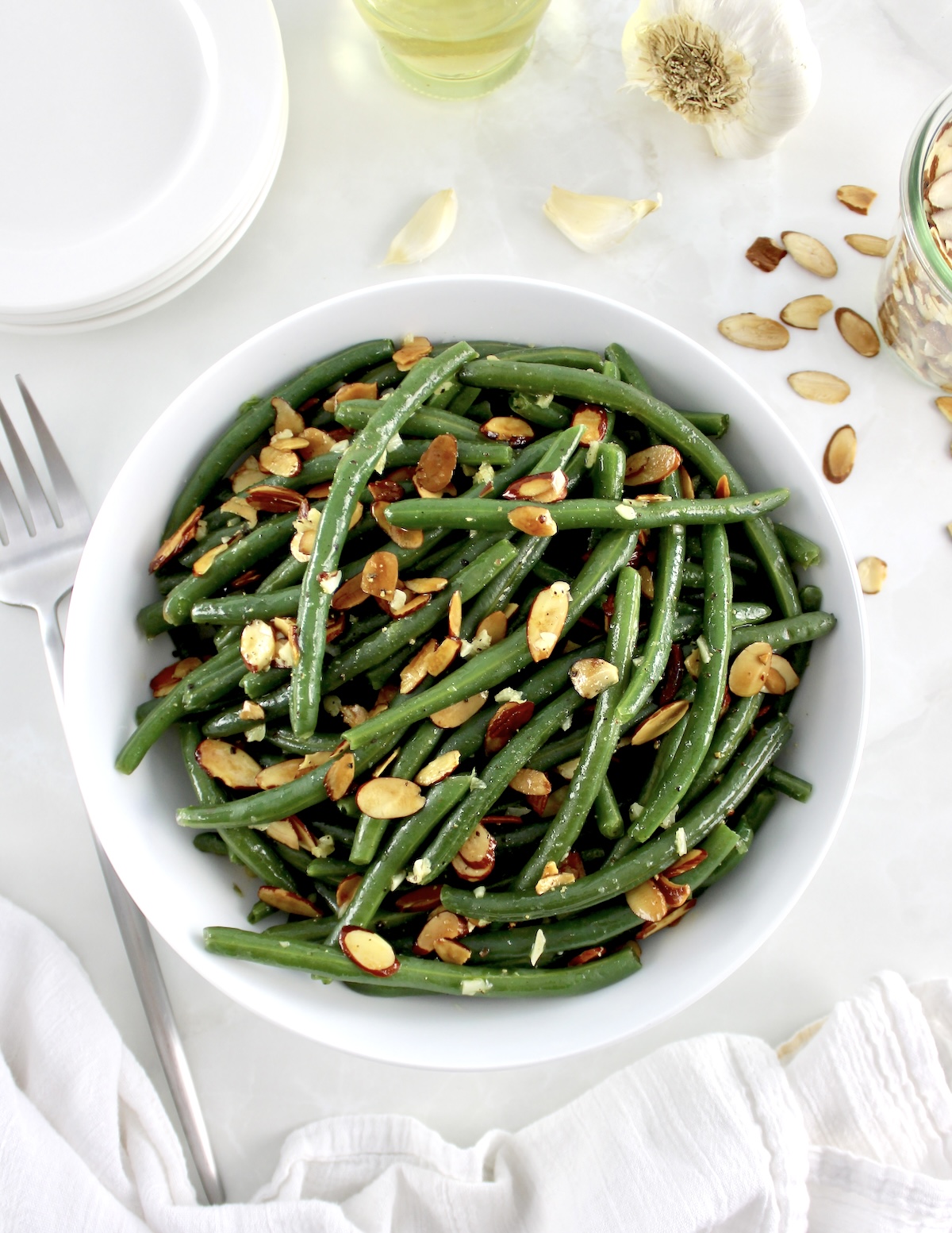 overhead view of Green Beans Almondine in white bowl with serving fork on side