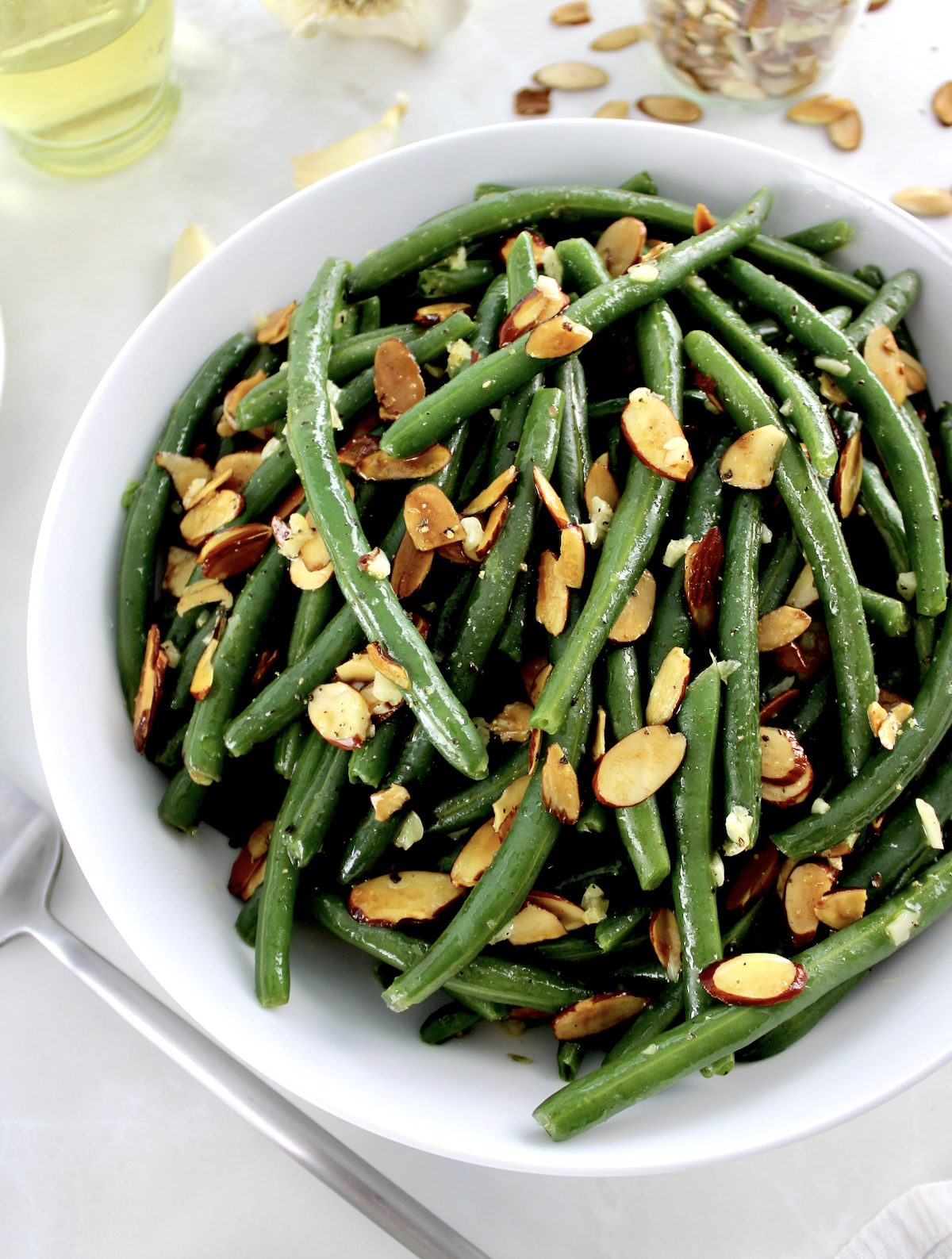overhead view of Green Beans Almondine in white bowl with serving spoon on side