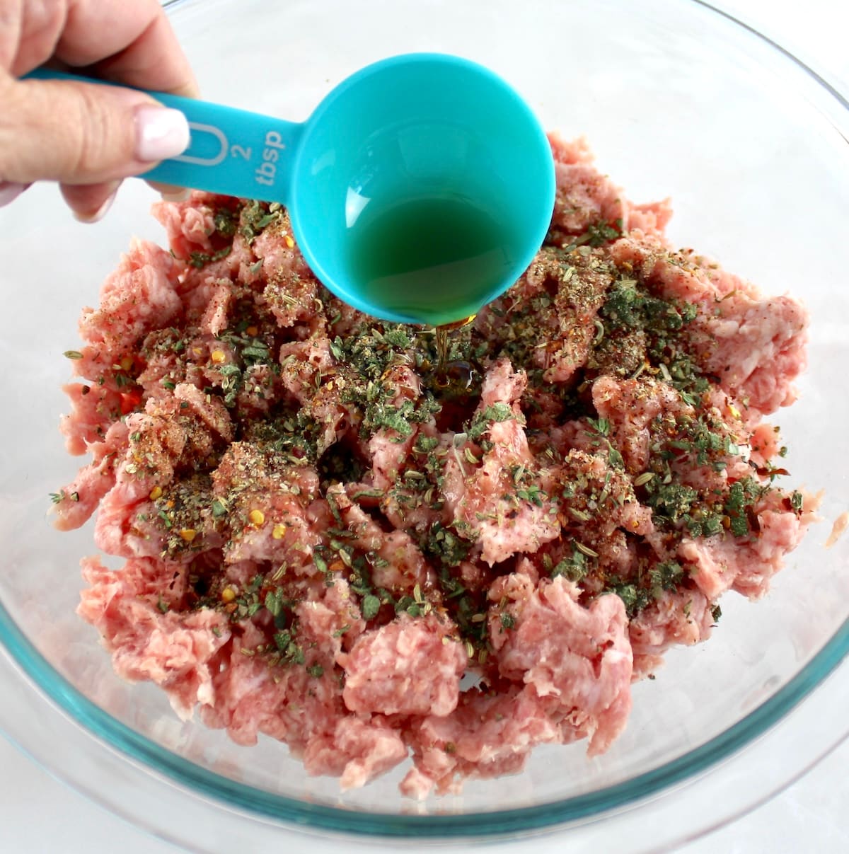 sugar free maple syrup pouring over ground pork and spices in glass bowl