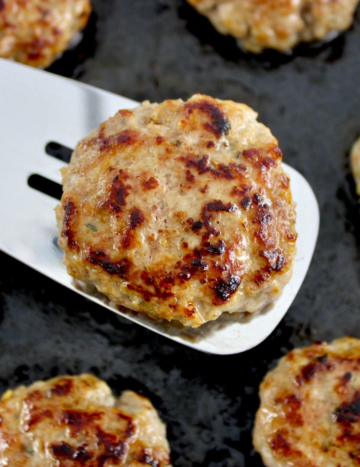 Homemade Breakfast Sausage held up on silver spatula over frying pan