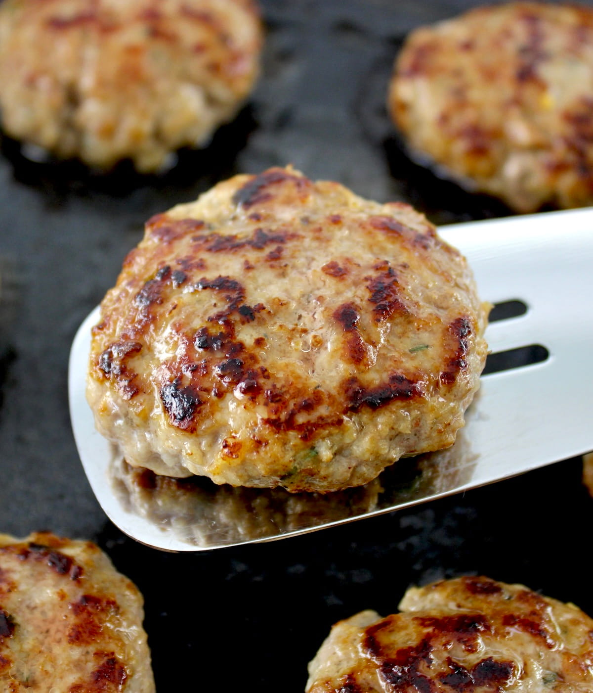 Homemade Breakfast Sausage patty on silver spatula held up over skillet