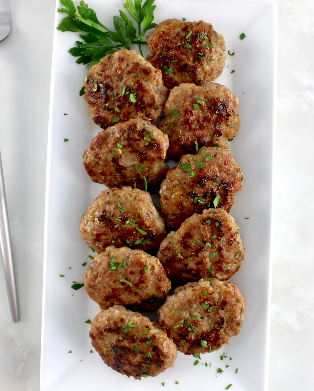 overhead view of Homemade Breakfast Sausage patties lined up on white rectangular plate with fresh parsley garnish