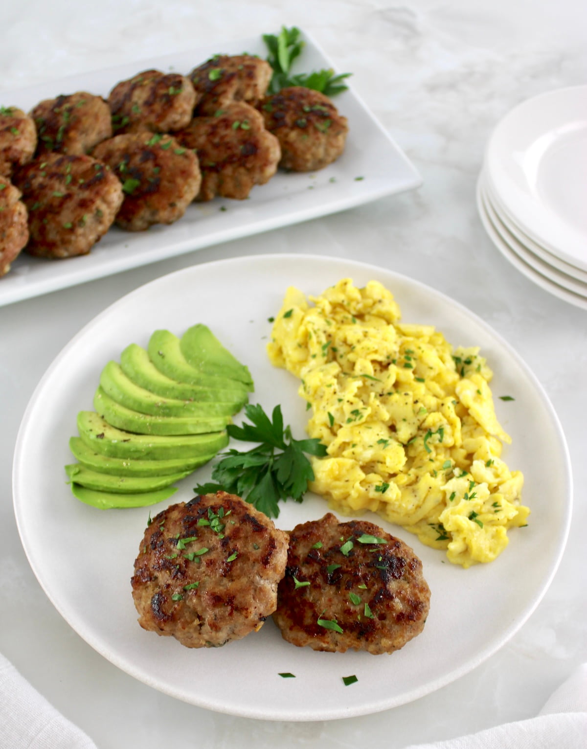 2 Homemade Breakfast Sausages on plate with scrambled eggs and sliced avocado