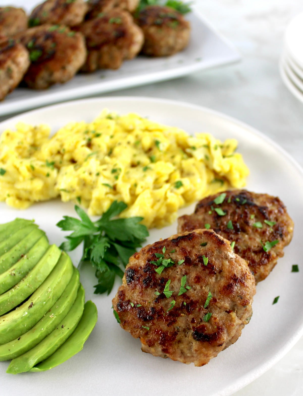 2 Homemade Breakfast Sausages on plate with scrambled eggs and sliced avocado