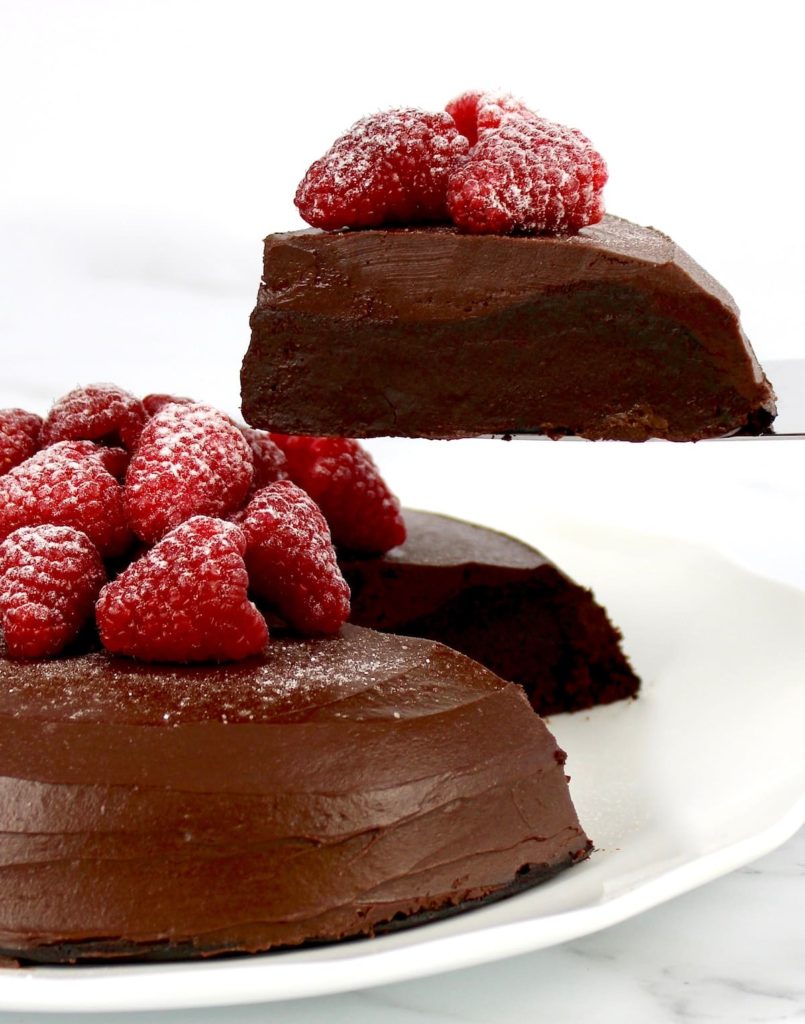 chocolate cake with raspberries on top with slice held up