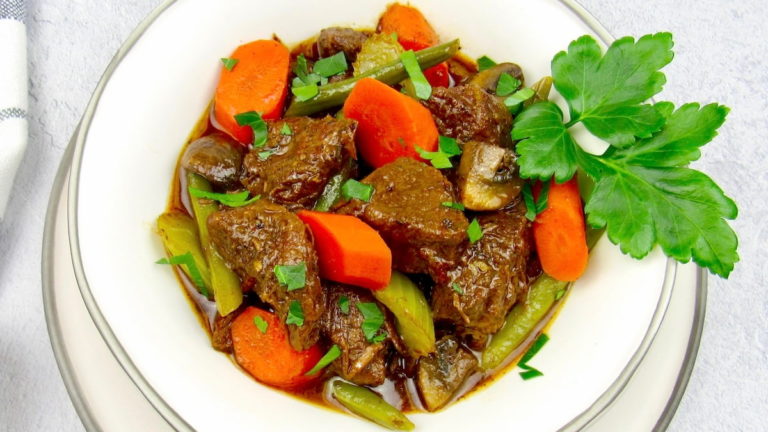 closeup of instant pot beef stew in white bowl with parsley garnish
