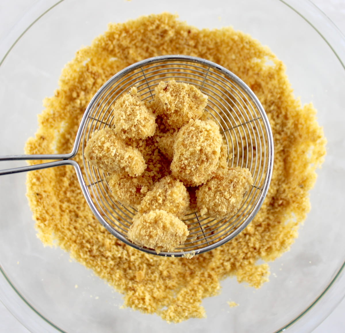 uncooked Keto Popcorn Chicken in spider held up over bowl with breading