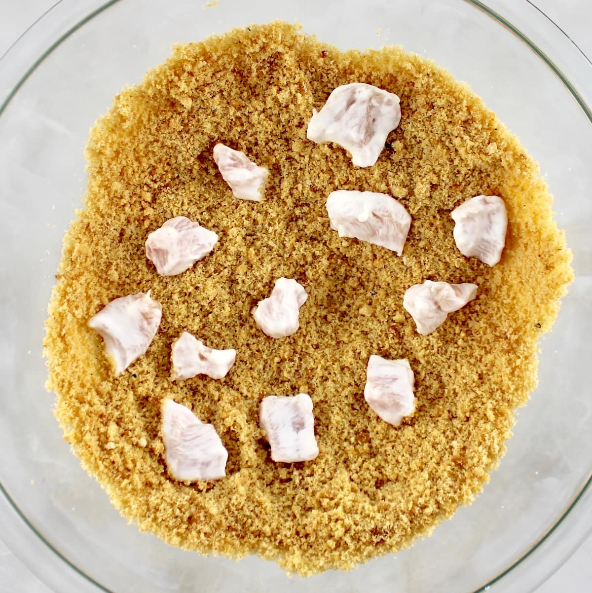 small pieces of chicken sitting in breading in glass bowl