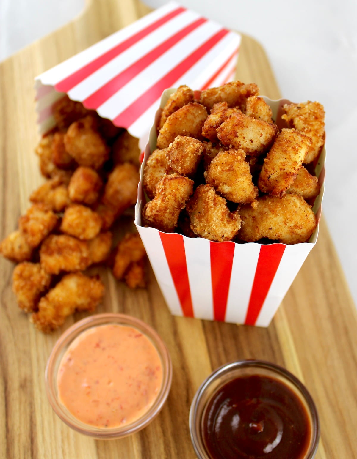 overhead view of 2 containers of Keto Popcorn Chicken on cutting board with dipping sauces on side