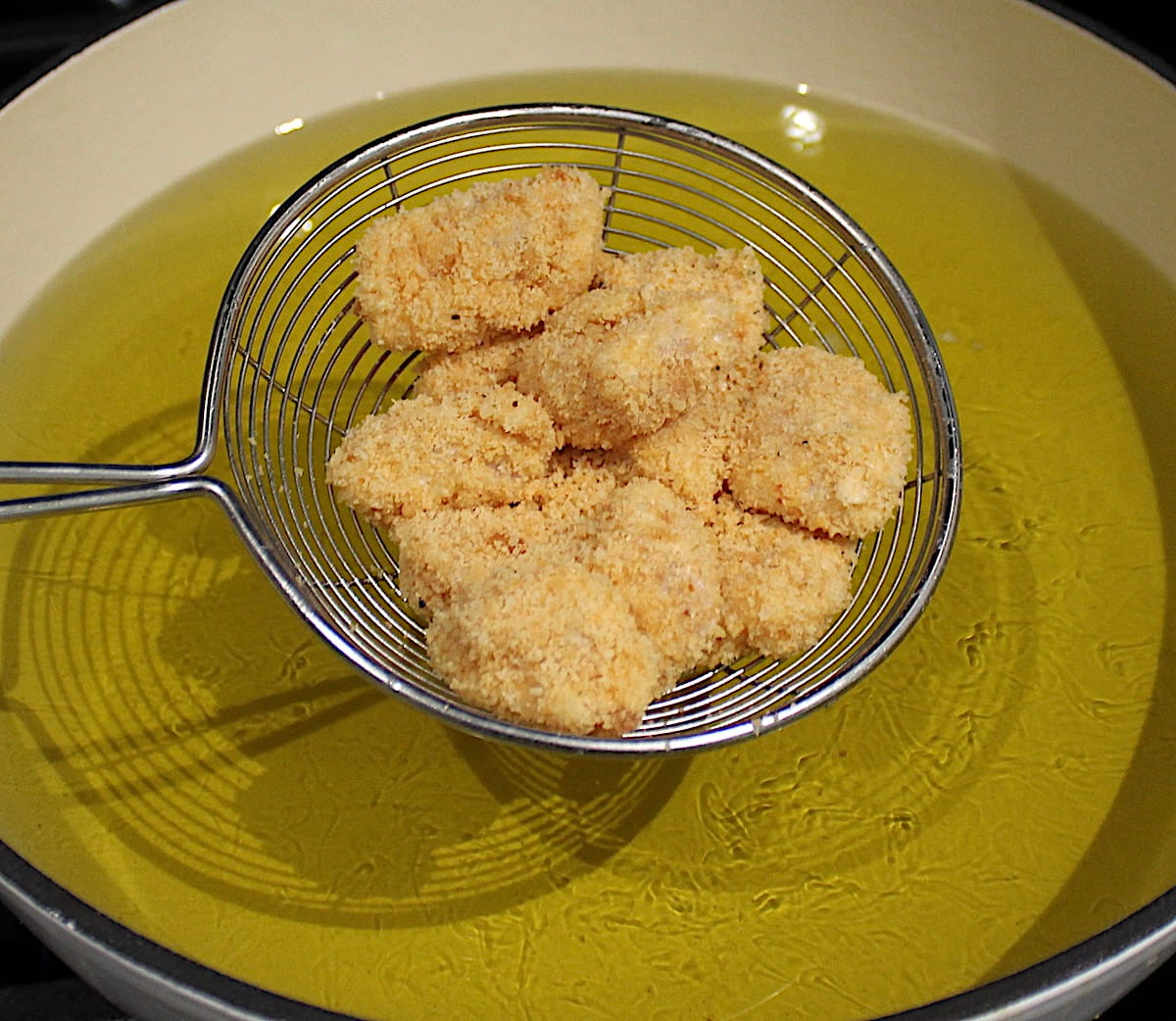 Keto Popcorn Chicken in spider held up over pot with oil