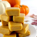 Keto Pumpkin Fudge stacked up on white plate with pumpkins in back