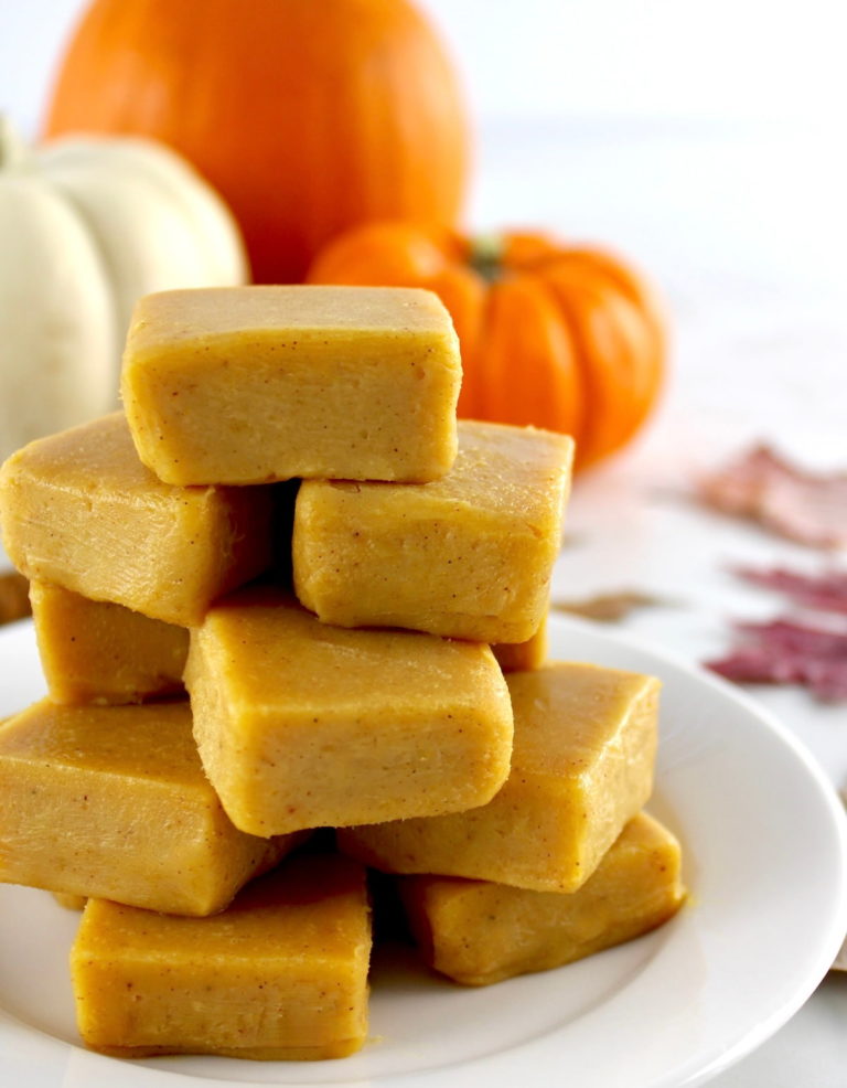 Keto Pumpkin Fudge stacked up on white plate with pumpkins in back