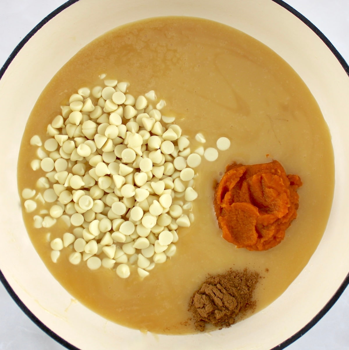 keto sweetened condensed milk in pot with white chocolate chips, pumpkin puree and spice unmixed