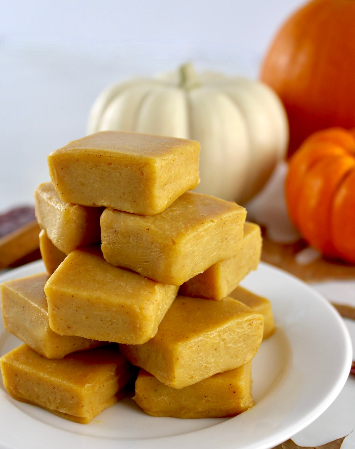 Keto Pumpkin Fudge stacked up on white plate with pumpkins in background
