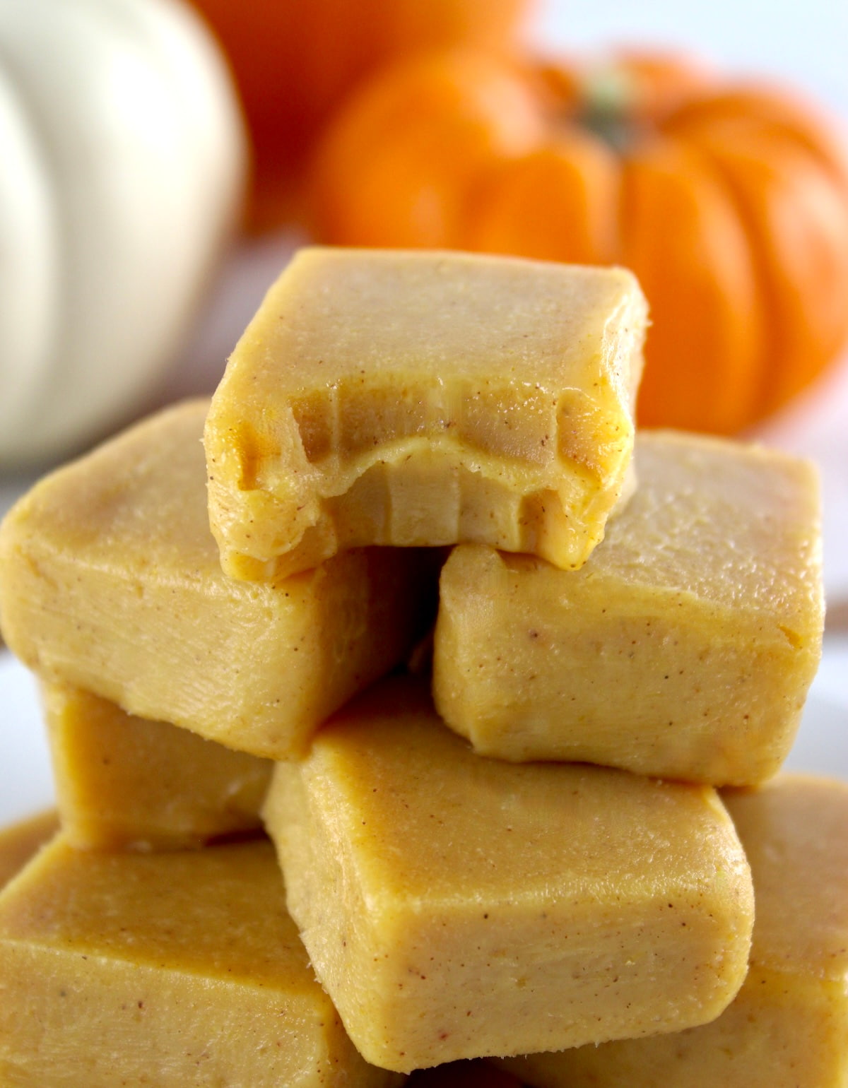 Keto Pumpkin Fudge stacked up with bite missing on top piece and pumpkins in back