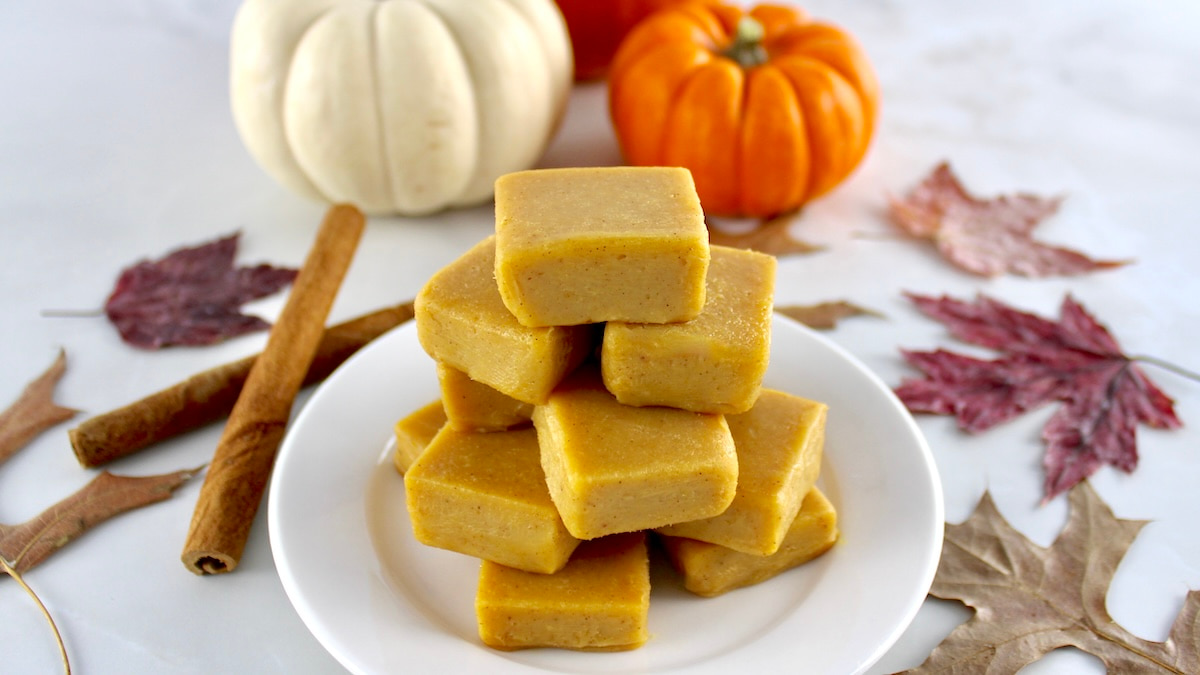 Keto Pumpkin Fudge stacked up on white plate with fall leaves and pumpkins in background