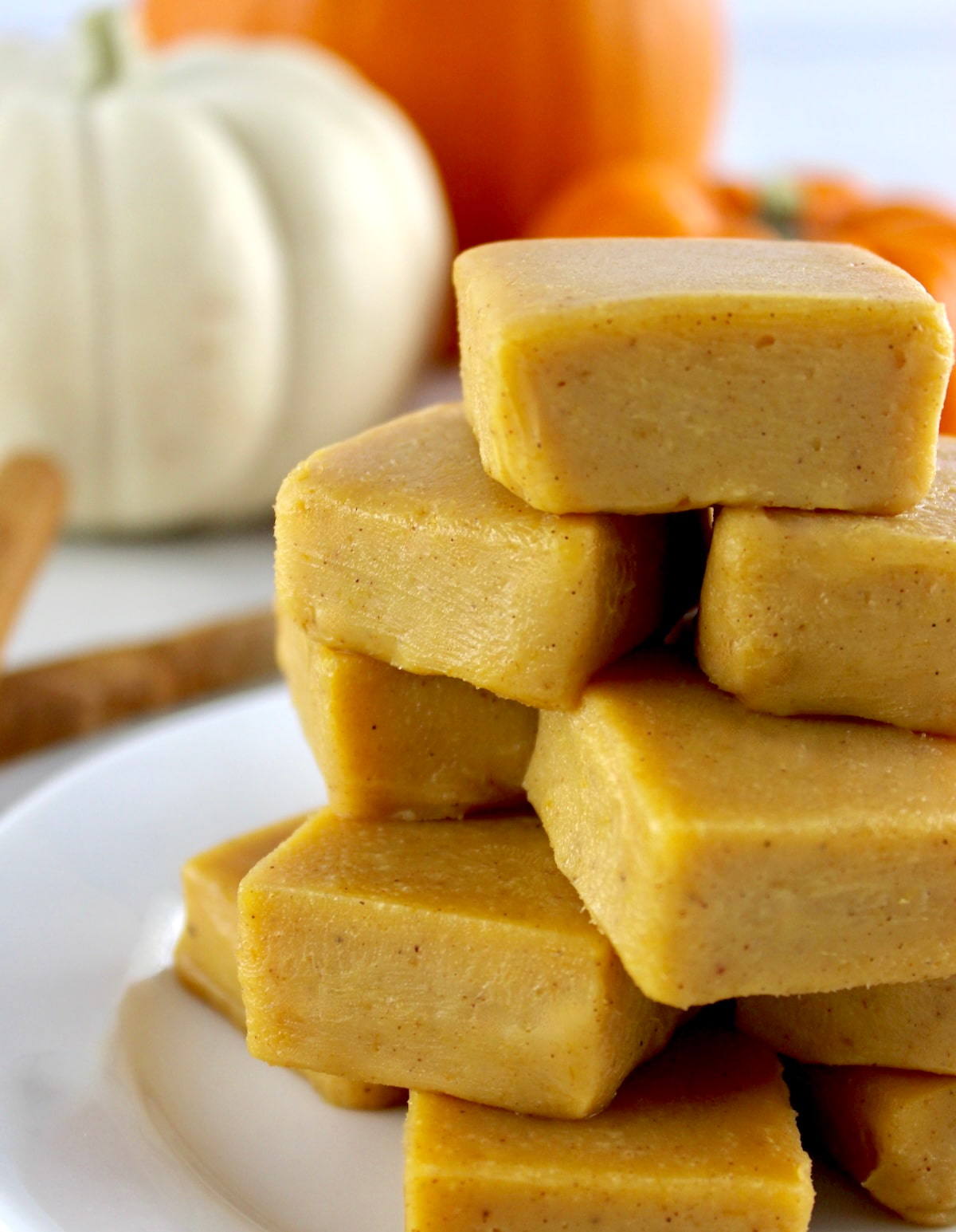 Keto Pumpkin Fudge stacked up on white plate with pumpkins in background
