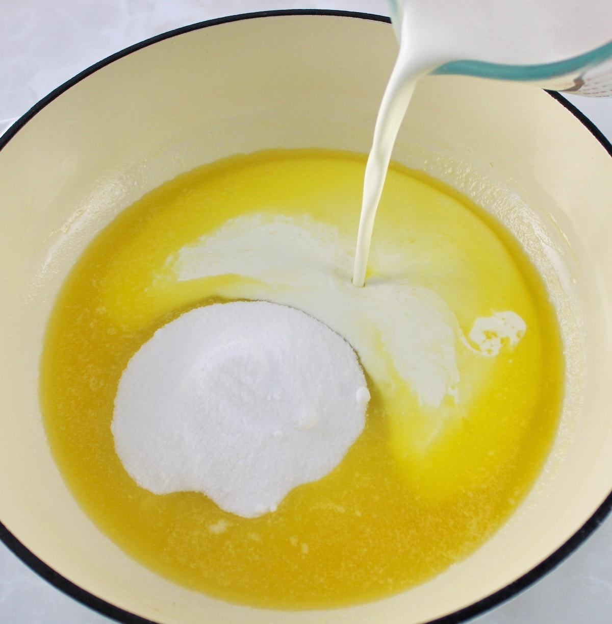 heavy cream being poured into pan with melted butter and sweetener