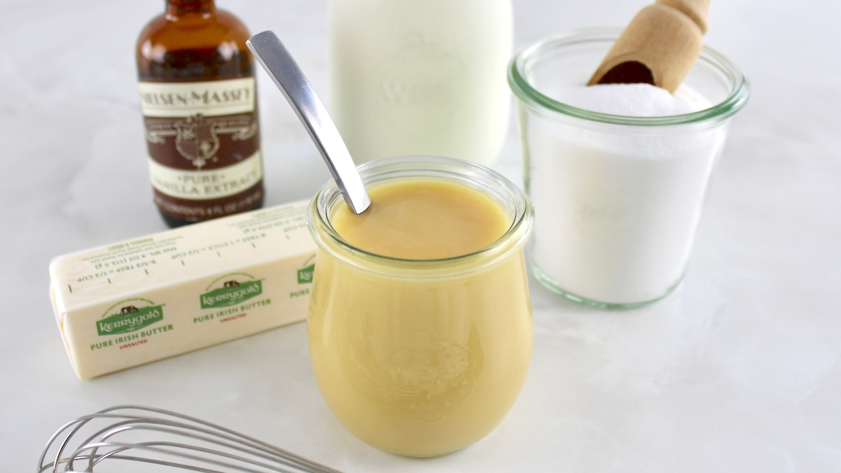 Keto Sweetened Condensed Milk in open glass jar with spoon and ingredients in back