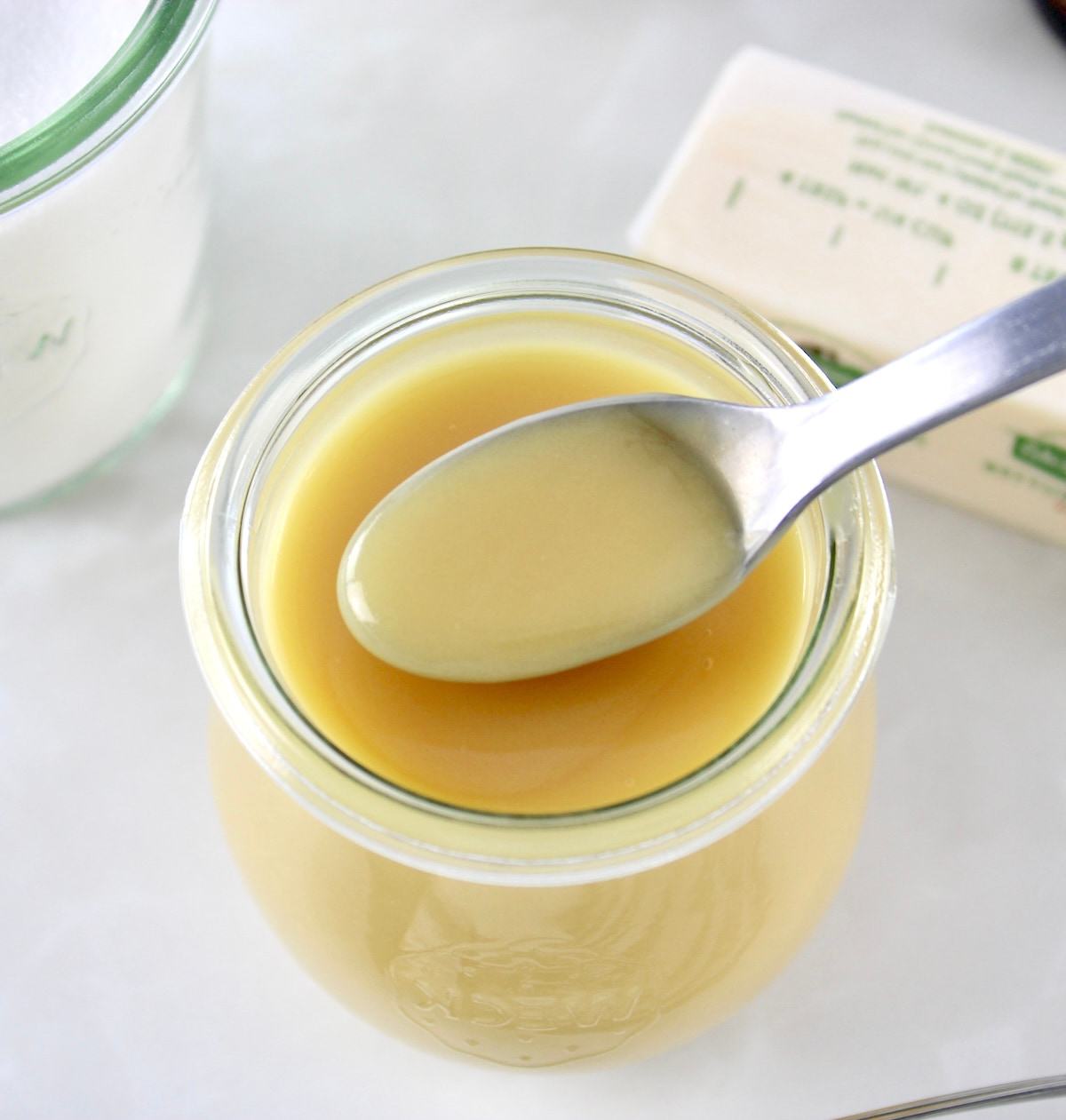 overhead view of Keto Sweetened Condensed Milk in spoon held up over glass jar