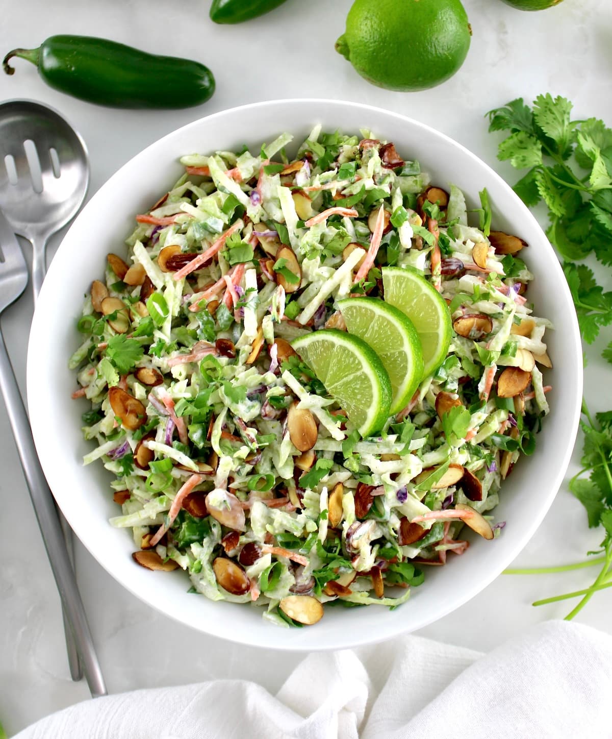 overhead view of Lime Cilantro Broccoli Slaw in white bowl with silver serving fork and spoon on side