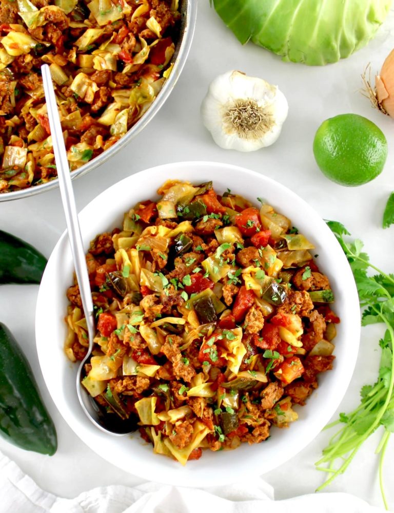 Mexican Chorizo and Cabbage in white bowl with silver spoon and skillet in back
