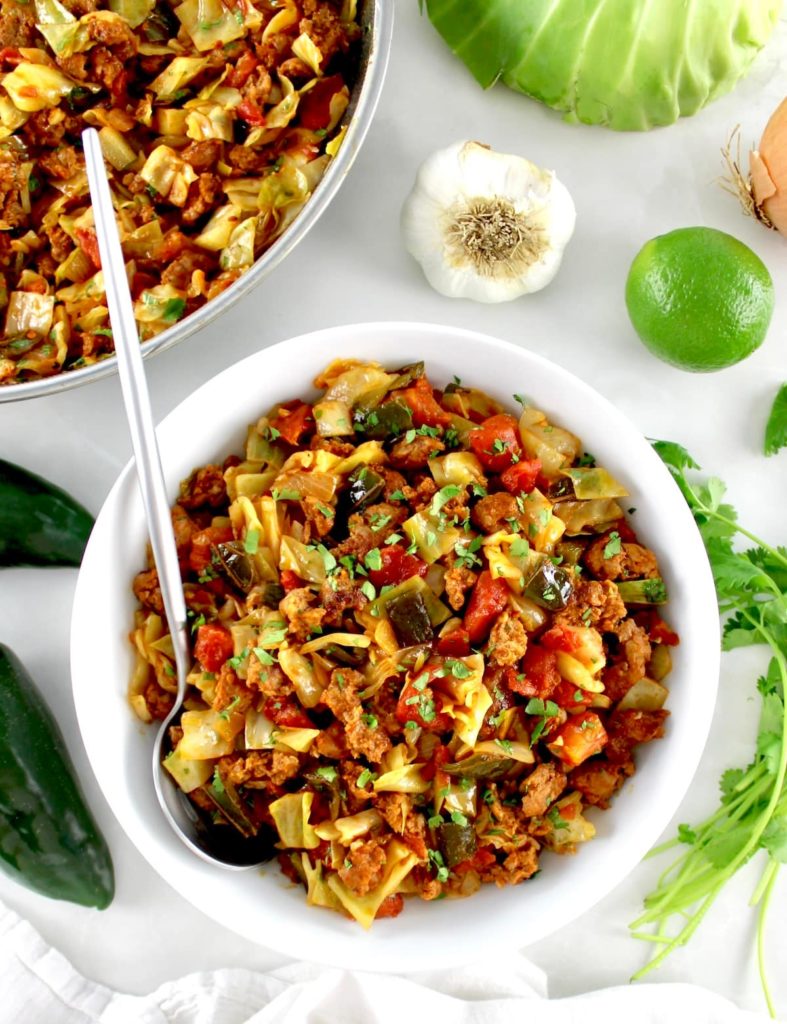 Mexican Chorizo and Cabbage in white bowl with silver spoon and skillet in back