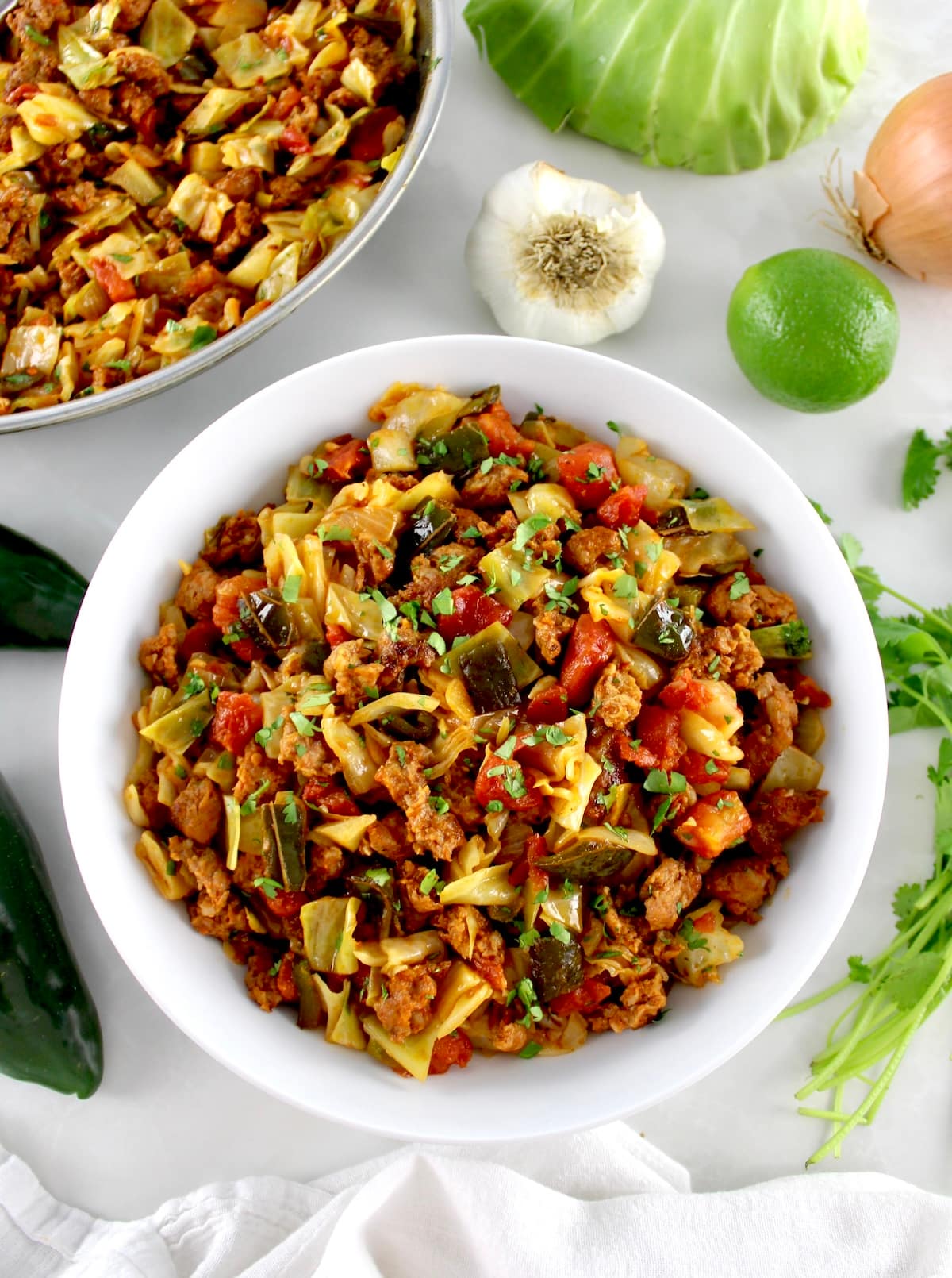 overhead view of Mexican Chorizo and Cabbage in white bowl with skillet in back