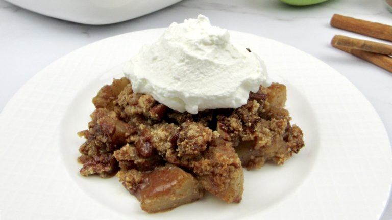 apple crumble topped with whipped cream on a round white plate