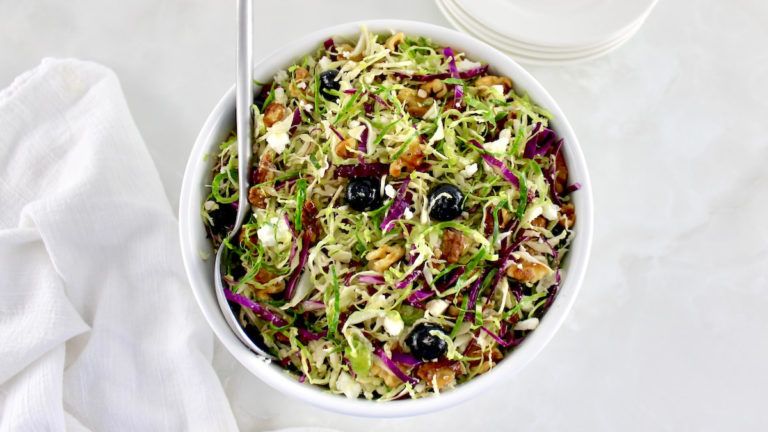 Shaved Brussels Sprouts Salad in white bowl with silver serving spoon on side