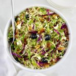 overhead view of Shaved Brussels Sprouts Salad in white bowl with serving spoon on side