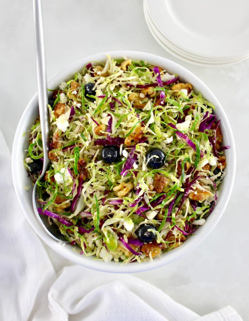 overhead view of Shaved Brussels Sprouts Salad in white bowl with serving spoon on side