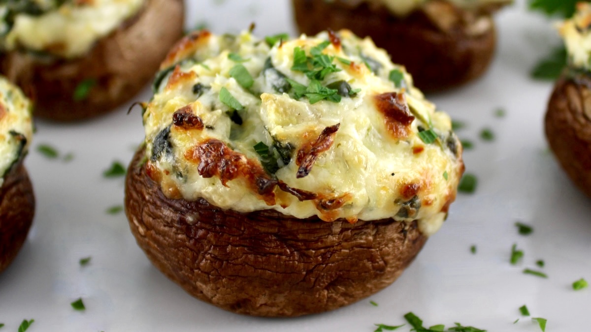 closeup of Spinach Artichoke Stuffed Mushrooms on white plate with parsley