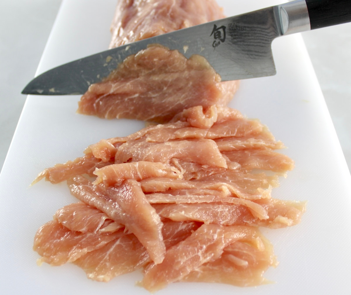 pork tenderloin on white cutting board being sliced thinly