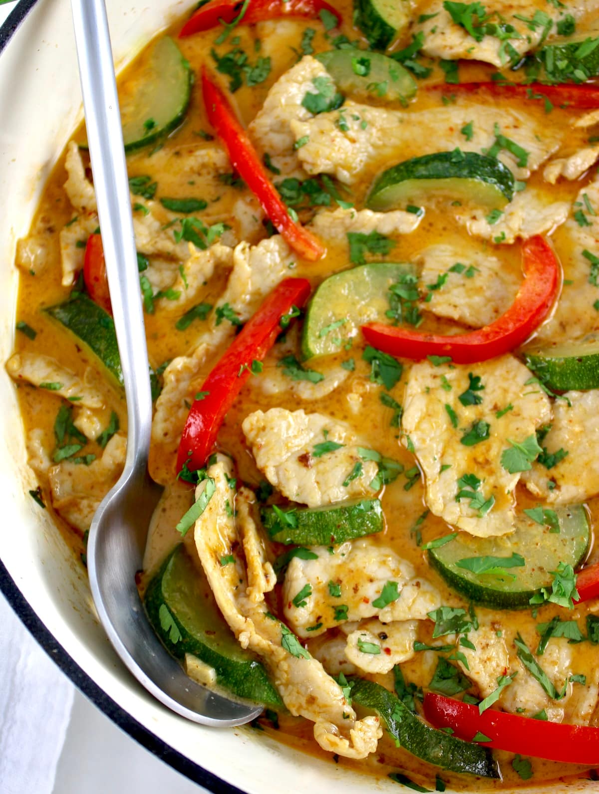 closeup of Thai Red Curry Coconut Pork in white pan with silver serving spoon on side