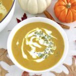 overhead view of Easy Pumpkin Soup in white bowl with pumpkins and fall leaves in back