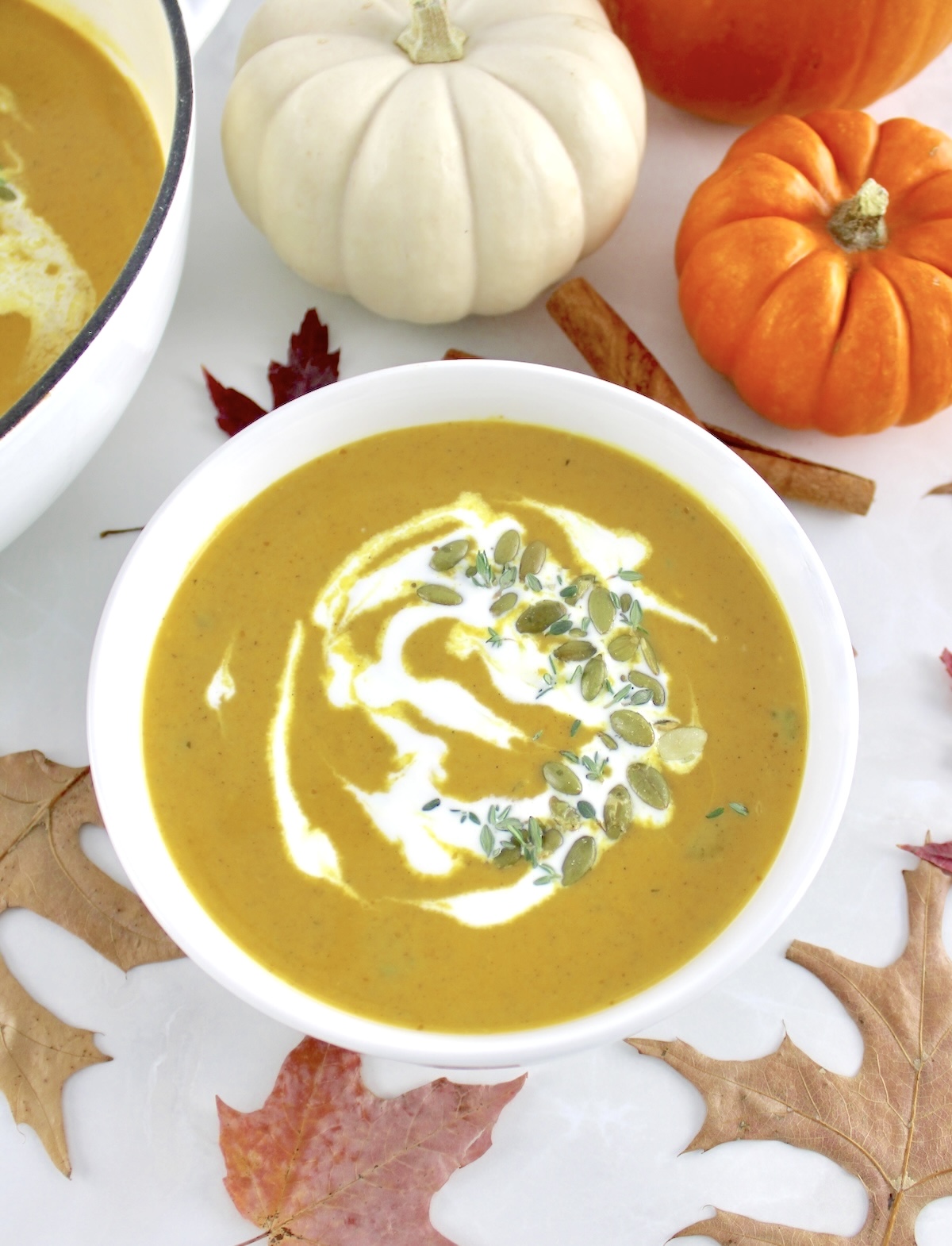 overhead view of Easy Pumpkin Soup in white bowl with pumpkins and fall leaves in back