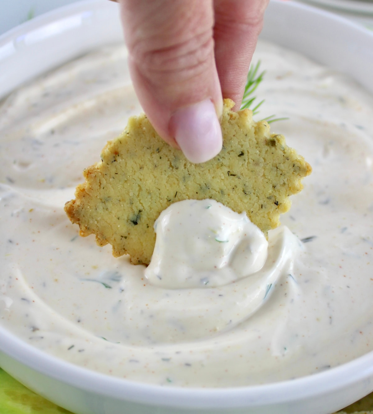 dipping Keto cracker in Easy Veggie Dip in white bowl